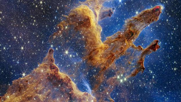 Pillars of Creation captured in NASAs James Webb Space Telescopes near-infrared view. The pillars resemble arches and spires rising from a desert, but are filled with semitransparent gas and dust.